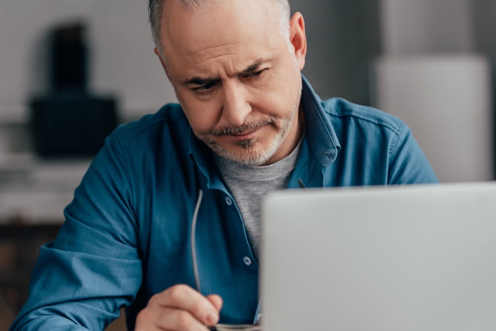 Unhappy man reviewing documents on a laptop, focusing on licensing and contractor certification.