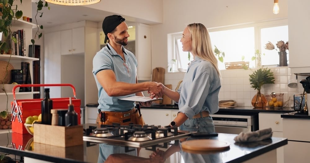 Friendly handshake between a repair technician and a satisfied customer in a modern kitchen.