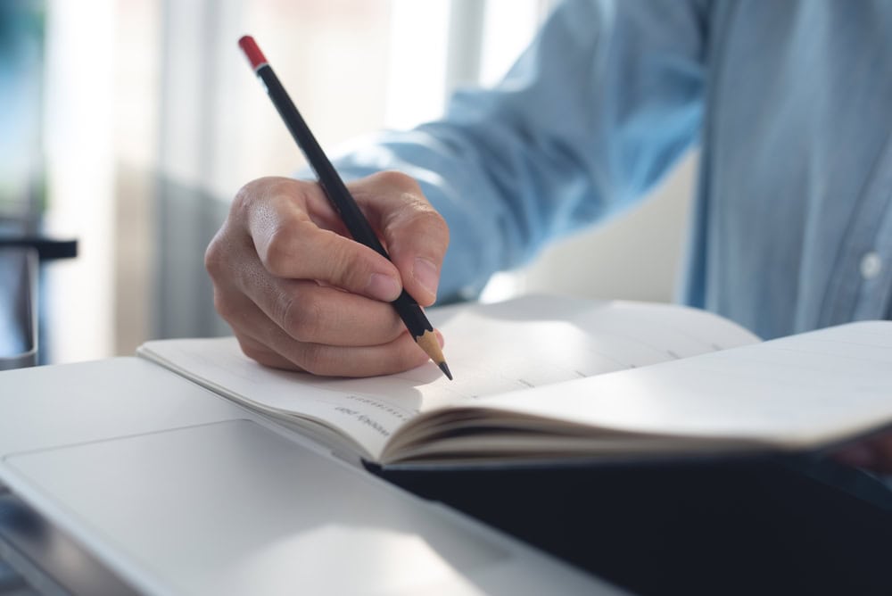 A person writing in a notebook with a pencil, focusing on planning or note-taking for a contractor business or project.