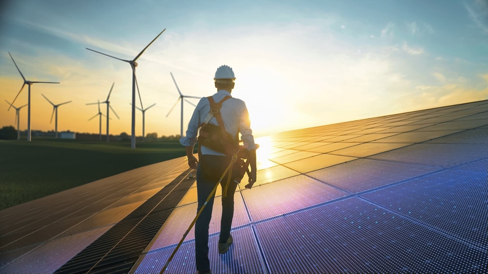 A construction worker inspecting solar panels and wind turbines at sunset, emphasizing renewable energy projects and sustainable construction practices.