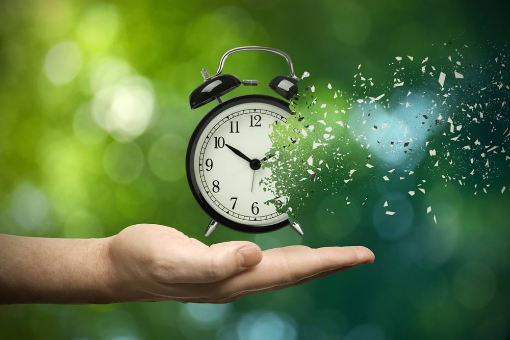 A hand holding a clock with a disintegrating effect, symbolizing time management and urgency in contractor licensing and training.