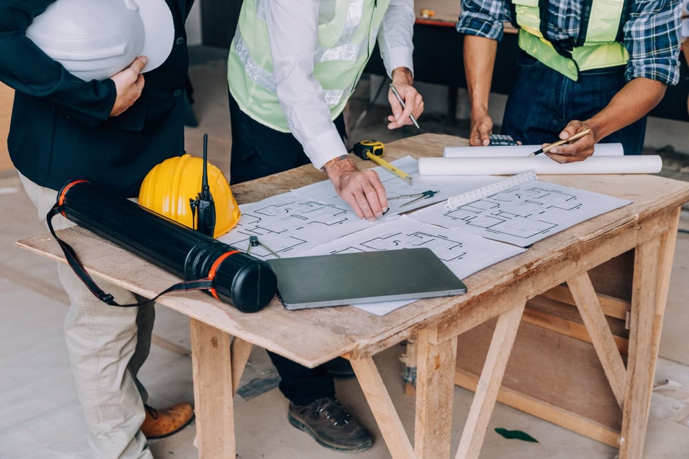Construction professionals reviewing blueprints and safety equipment on a work table, emphasizing contractor planning and project management.