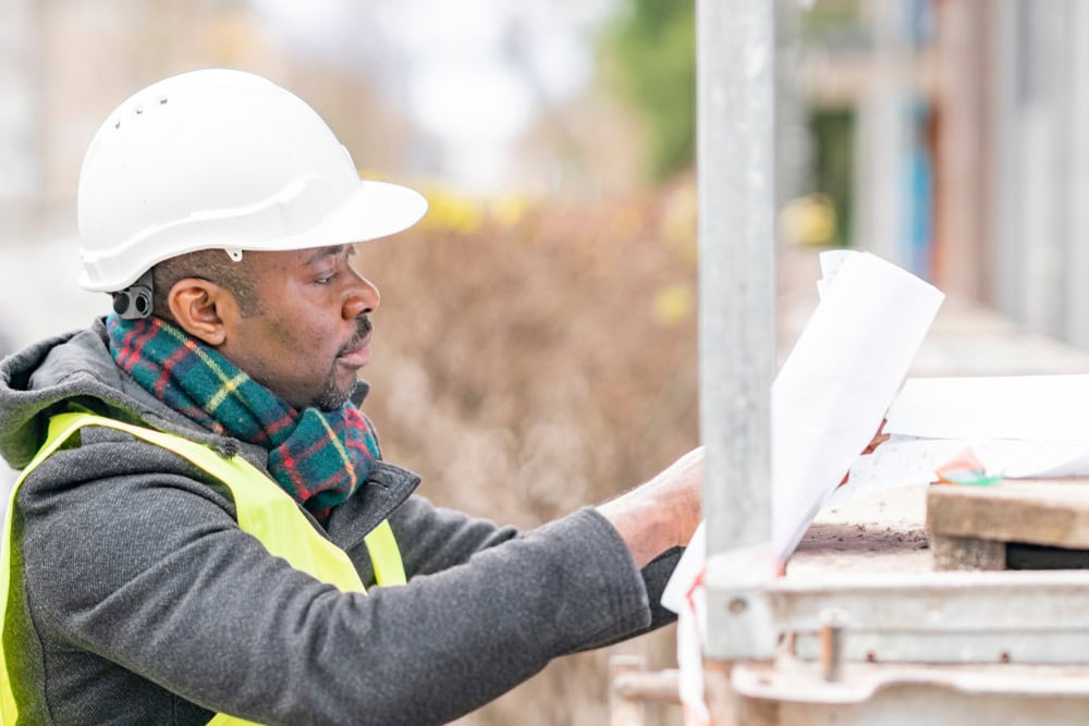 Construction worker in a white helmet reviewing blueprints at a construction site for contractor licensing and building projects.