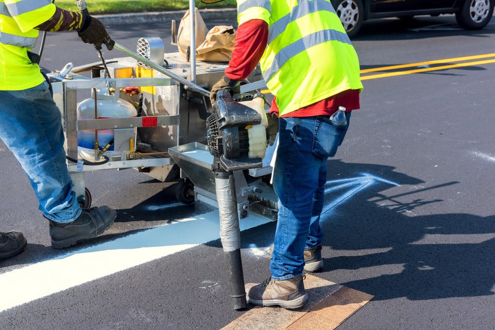 Road construction workers in safety vests using paving equipment to lay fresh asphalt on a city street.