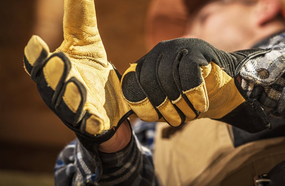 Close-up of a construction worker's hand giving a thumbs-up, wearing yellow and black work gloves, symbolizing safety and readiness in the construction industry.